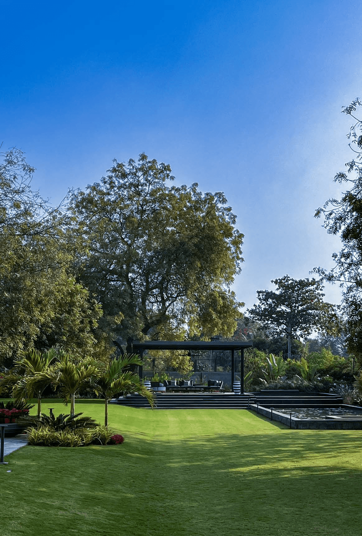 Grounds — manicured lawn, mature trees, outdoor pavilion with black steel canopy in distance