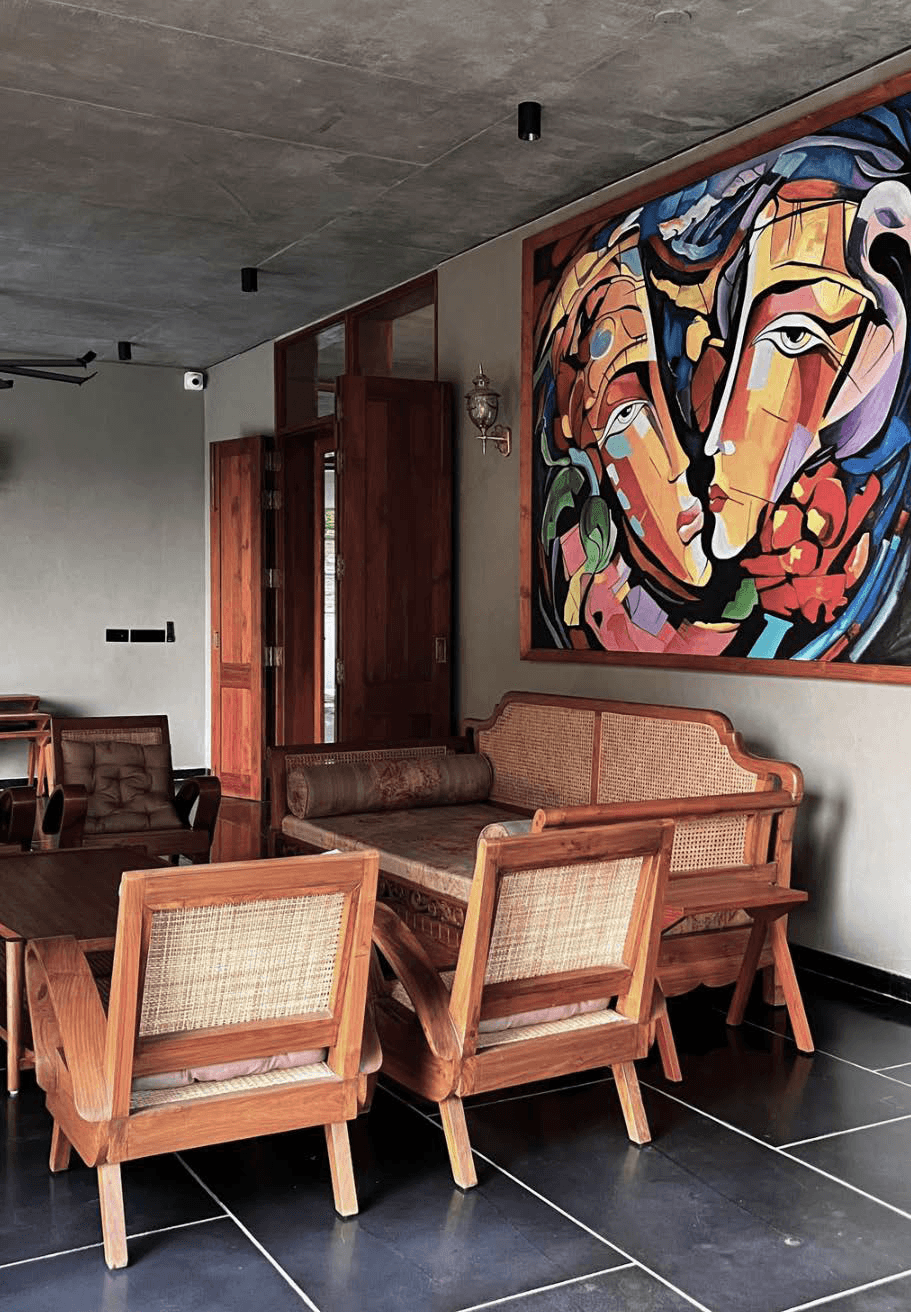 Sitting area — cane chairs, large figurative painting, exposed concrete ceiling