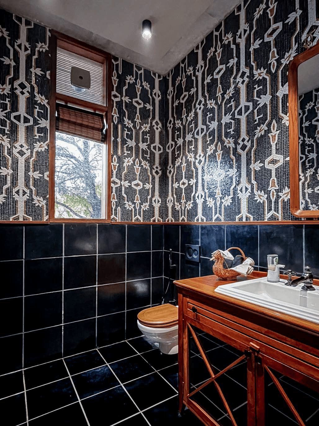 Powder room — floor-to-ceiling patterned mosaic wallpaper, black tile, teak vanity cabinet